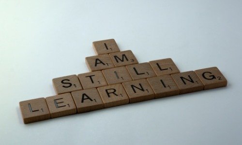 Scrabble letters on a white background that spell "I am still learning"