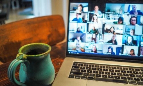 Laptop with various faces from a video call, with a green coffee mug sitting besides the screen.