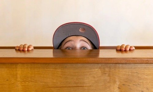 Man in a hat peeking over a desk