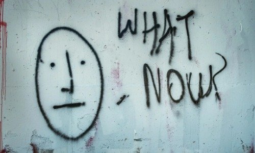 Graffiti art of a expressionless face with the words "What Now" next to it.